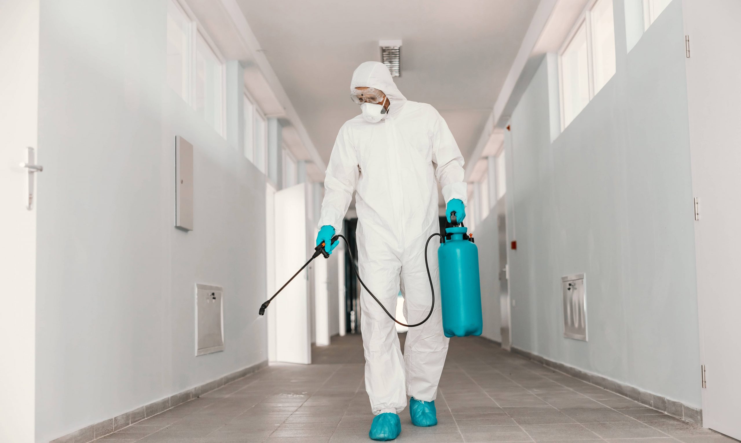 full-length-worker-sterile-uniform-with-face-mask-holding-sprayer-with-disinfectant-spraying-school-hallway